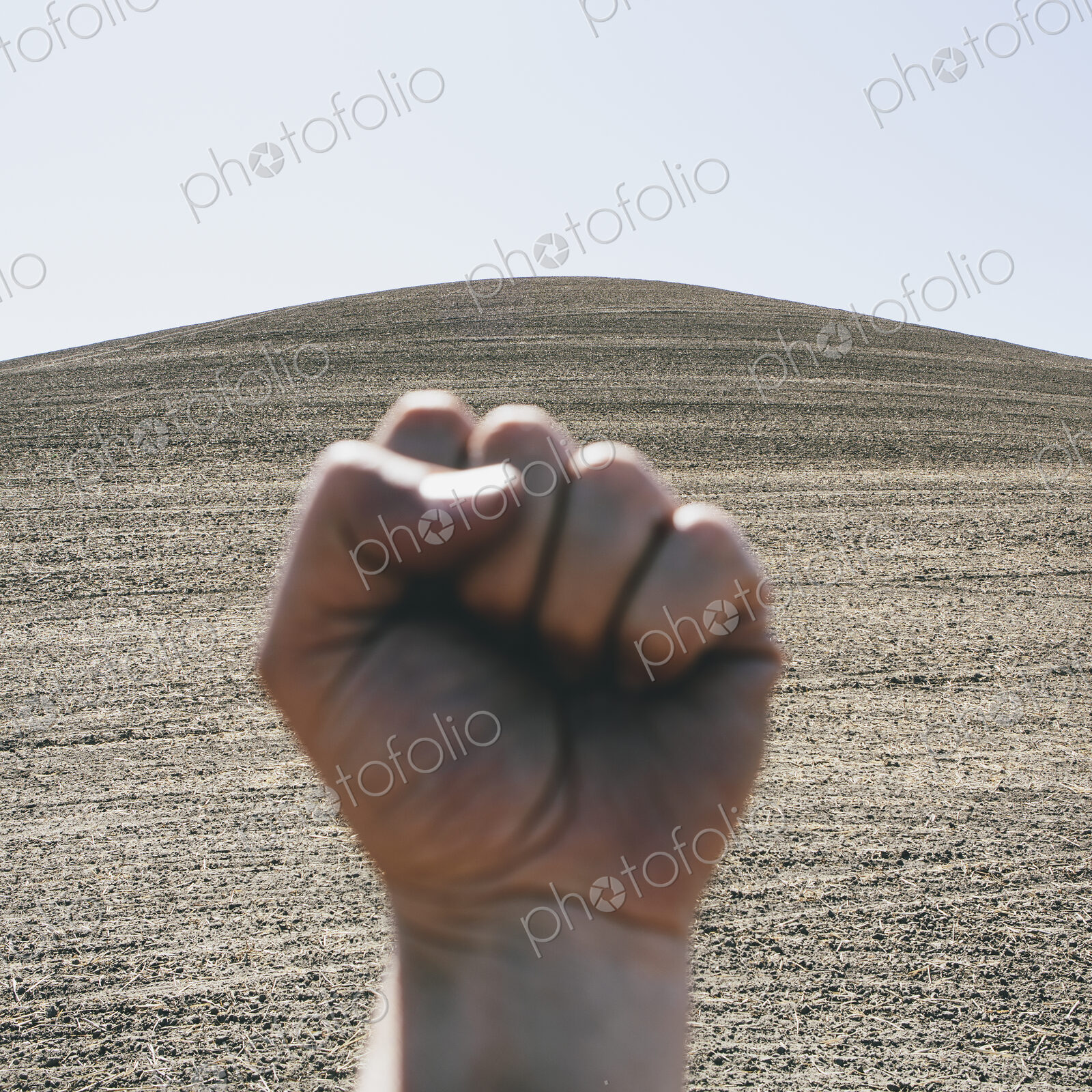 A hand bunched up and making fist, making a gesture. A ploughed field and farmland in…