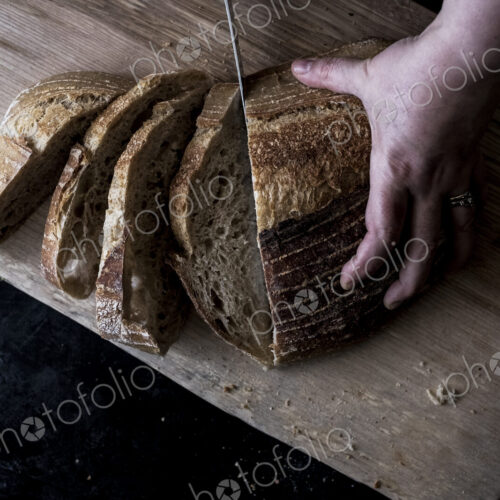 A hand holding a loaf of bread and using a breadknife to cut slces. A hand holding a loaf of bread and using a breadknife to cut slces.