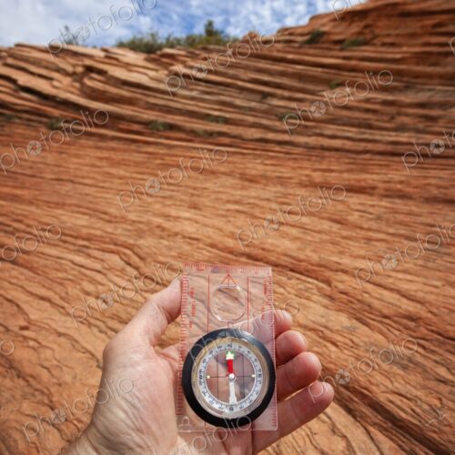 A hand holds a compass above wind-sculpted red sandstone in Zion National Park,… A hand holds a compass above wind-sculpted red sandstone in Zion National Park,…