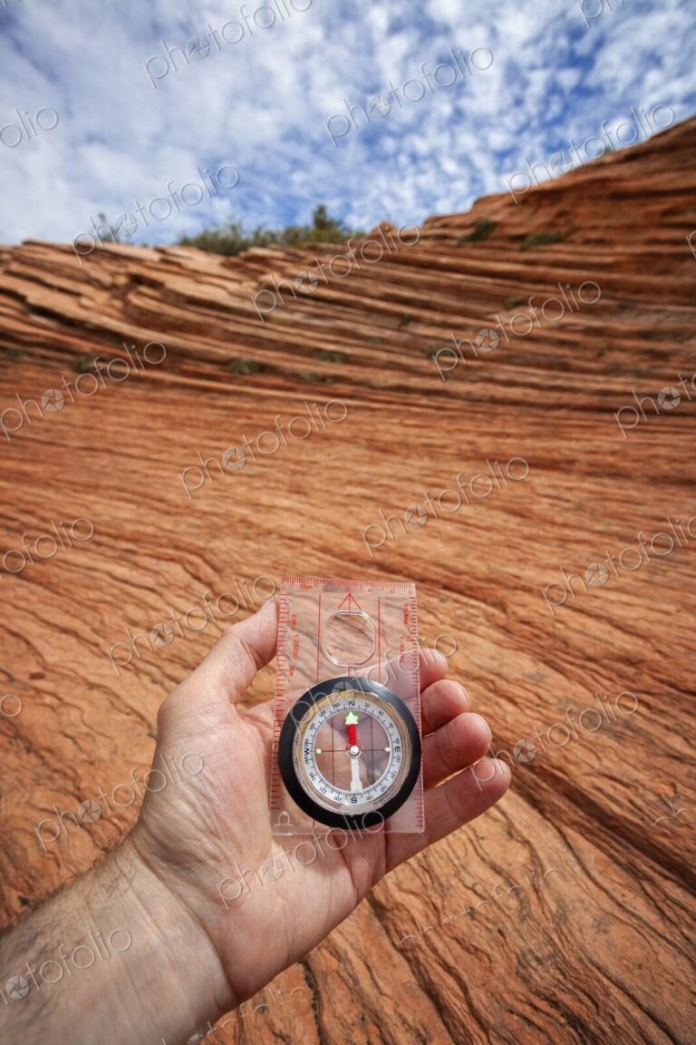 A hand holds a compass above wind-sculpted red sandstone in Zion National Park,…