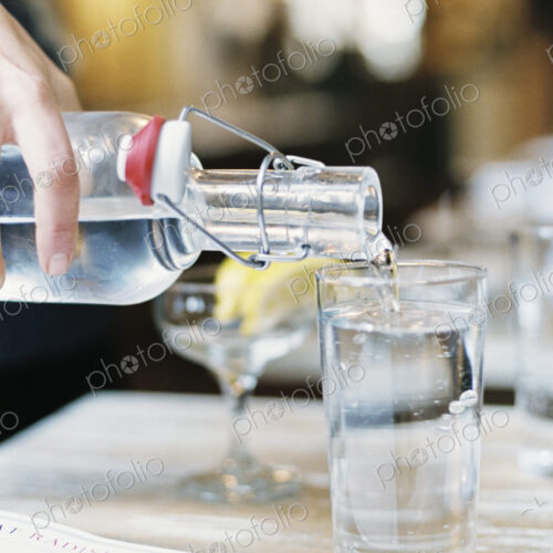 A hand pouring water from a bottle with a clip top into a glass. A hand pouring water from a bottle with a clip top into a glass.