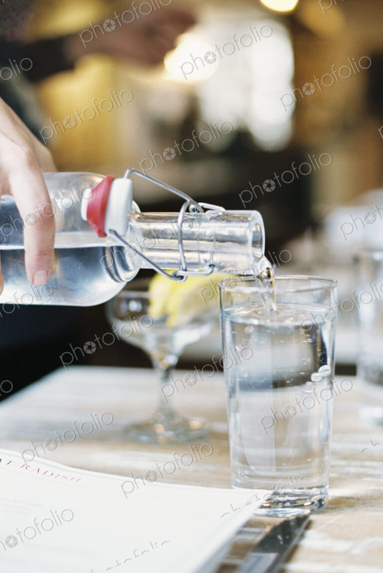 A hand pouring water from a bottle with a clip top into a glass.