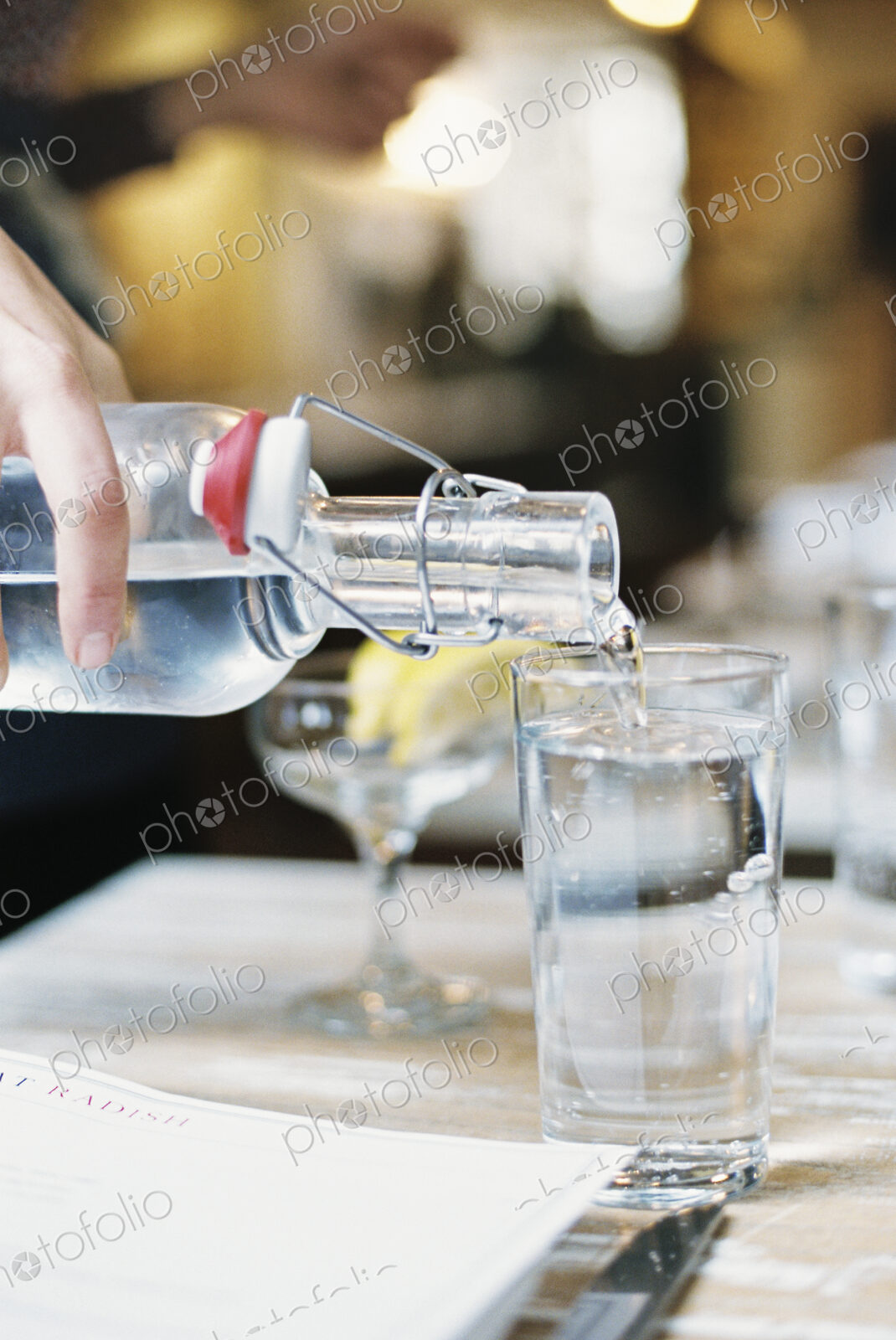 A hand pouring water from a bottle with a clip top into a glass.