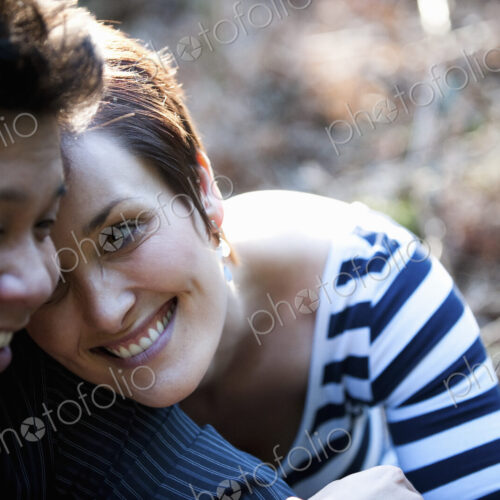 A happy couple sitting outdoors, heads touching and laughing.