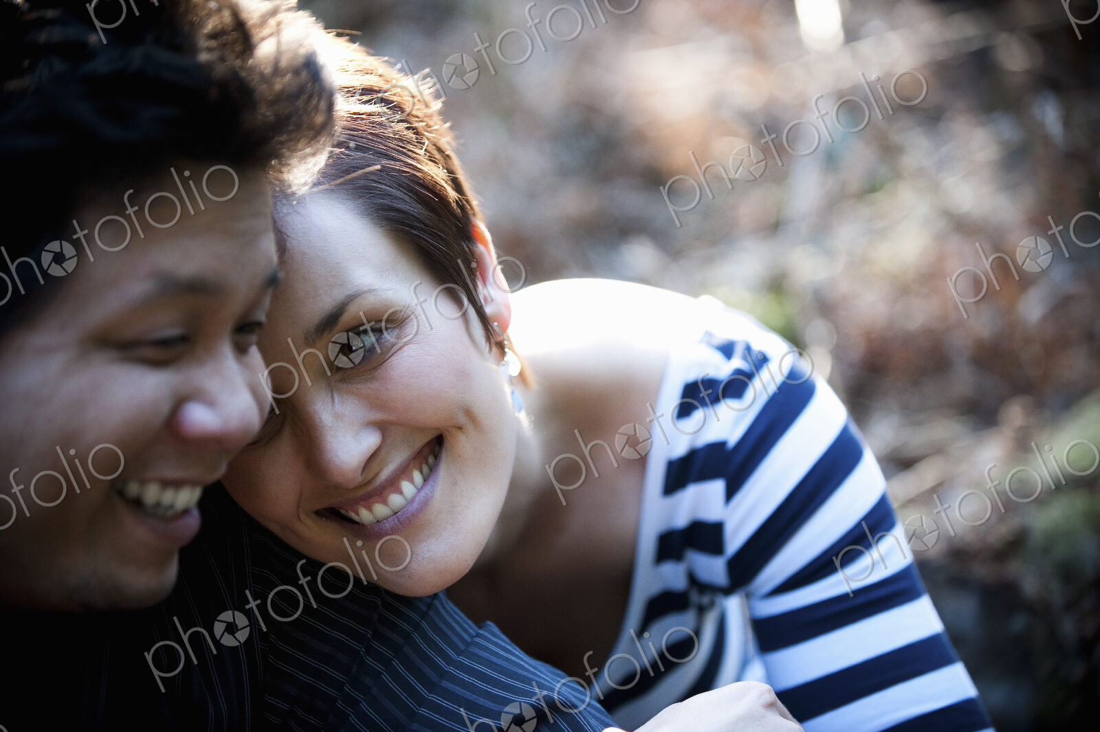 A happy couple sitting outdoors, heads touching and laughing.