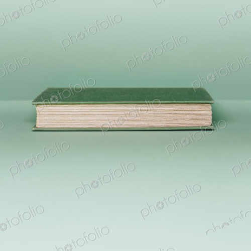 A hard cover book with a green cover, and white paper page edges, lying horizontal on…