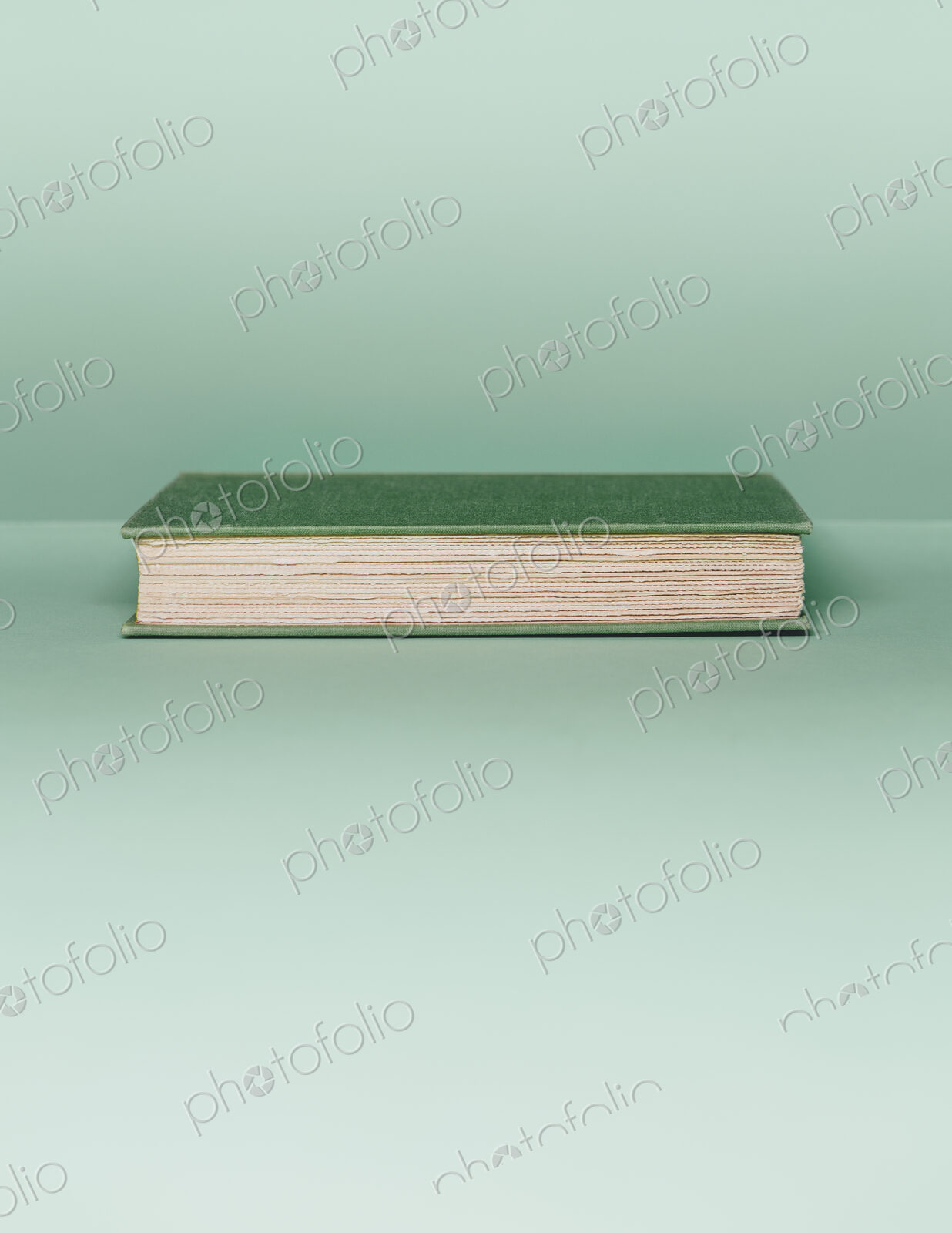 A hard cover book with a green cover, and white paper page edges, lying horizontal on…