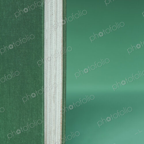 A hard cover book with a green cover, and white paper page edges, upright on a green…