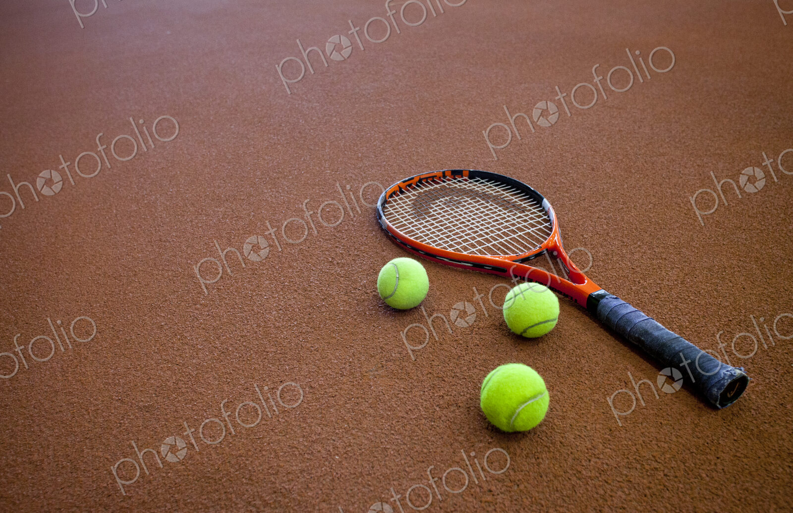 A hard tennis court and a tennis raquet,with three balls.