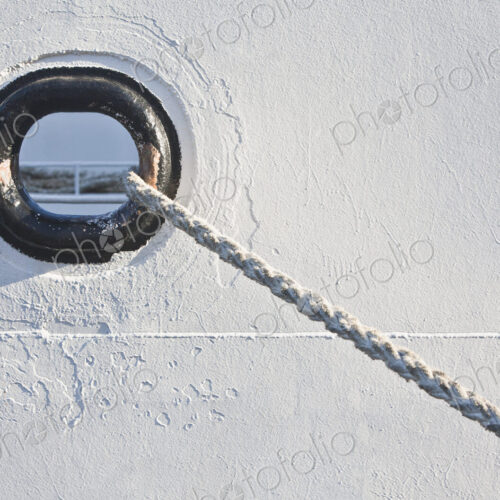 A hawser hole and hawser or mooring rope of a docked boat in a harbour.
