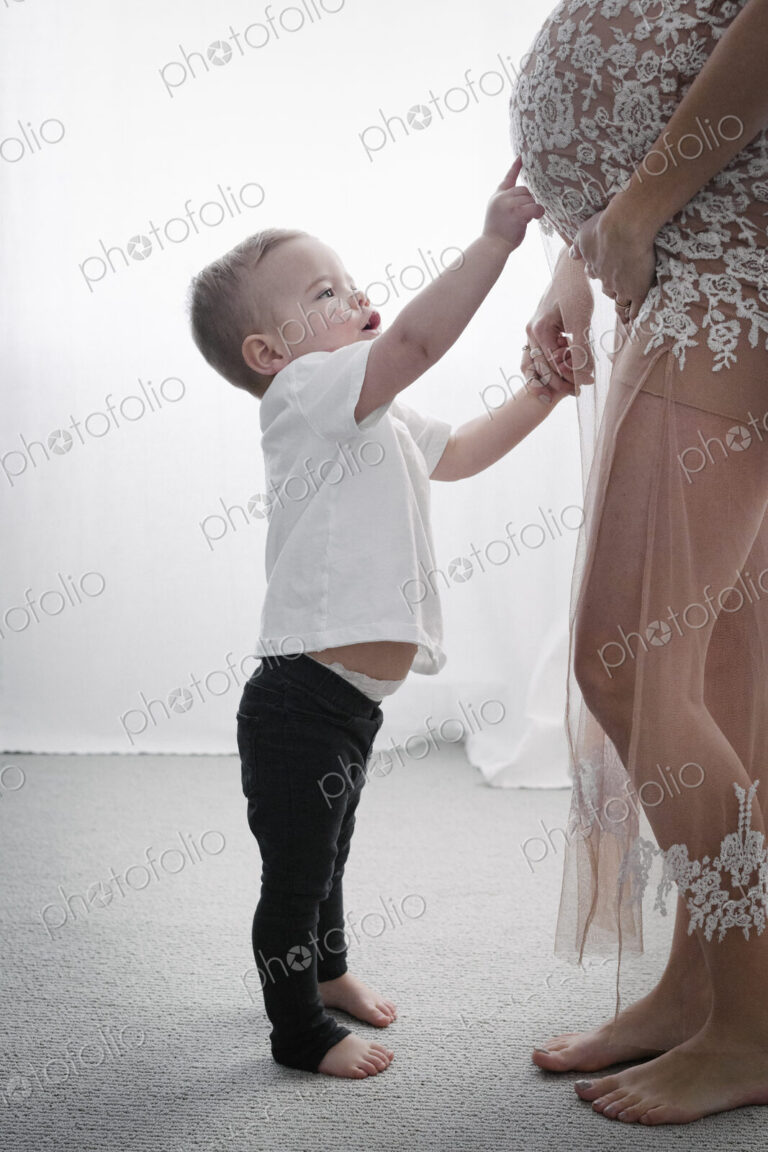 A heavily pregnant woman holding her young son by the hand.