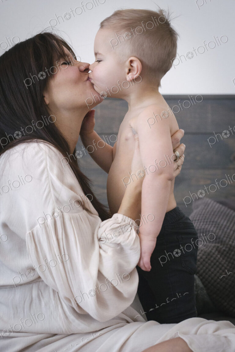 A heavily pregnant woman kissing her young son.