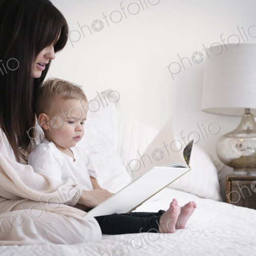 A heavily pregnant woman playing with her young son. Sitting on a bed, reading a story.