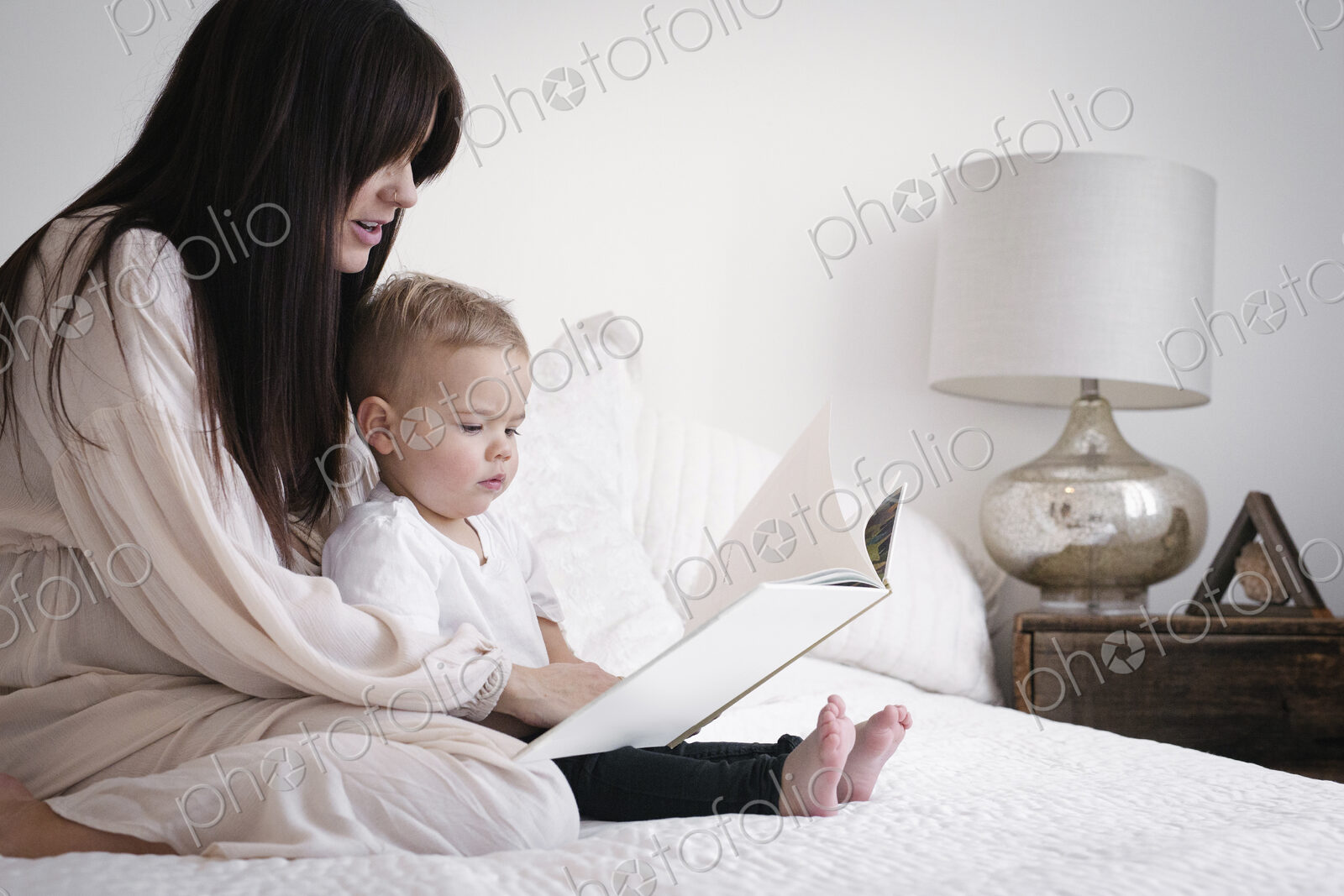 A heavily pregnant woman playing with her young son. Sitting on a bed, reading a story.