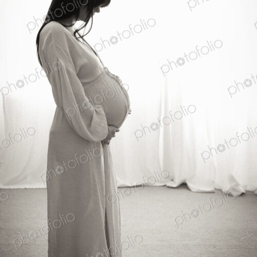 A heavily pregnant woman with her hands on her stomach seen in profile.