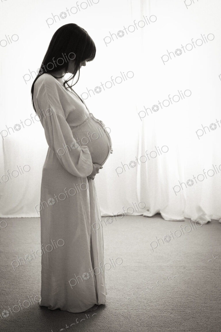 A heavily pregnant woman with her hands on her stomach seen in profile.