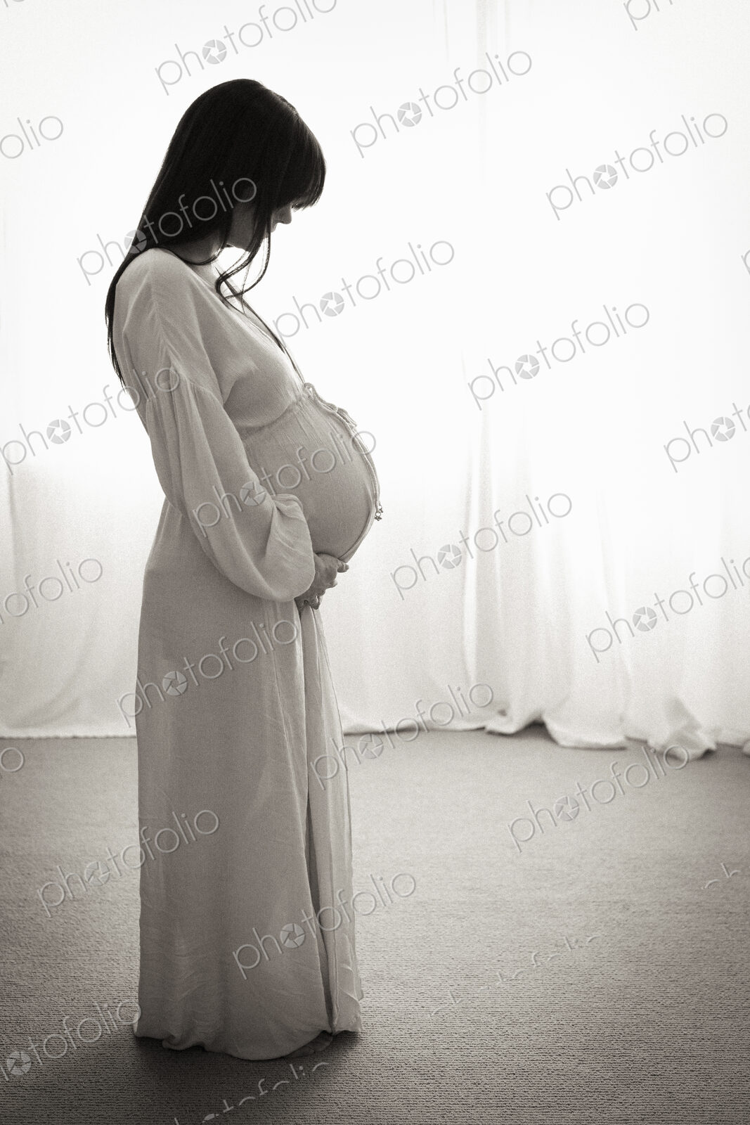 A heavily pregnant woman with her hands on her stomach seen in profile.