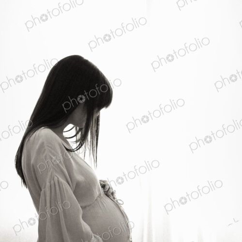 A heavily pregnant woman with her hands on her stomach seen in profile.