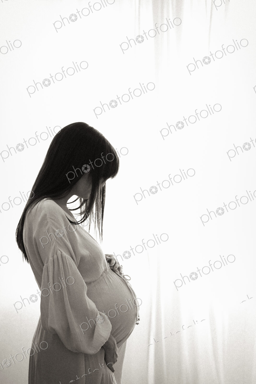 A heavily pregnant woman with her hands on her stomach seen in profile.