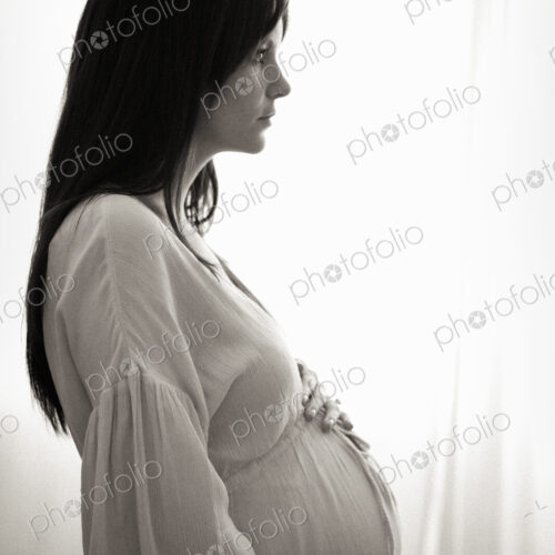 A heavily pregnant woman with her hands on her stomach seen in profile.