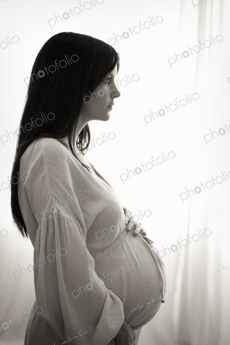 A heavily pregnant woman with her hands on her stomach seen in profile.