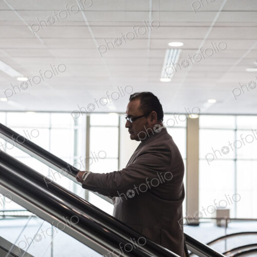 A hispanic businessman checking his notebook computer on an escalator A hispanic businessman checking his notebook computer on an escalator