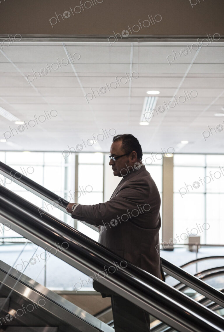 A hispanic businessman checking his notebook computer on an escalator