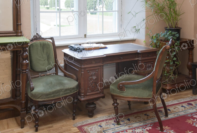 A historic house, antique furniture by a window, a desk and two chairs, window and…