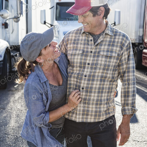 A husband and wife truck driving team near their truck parked in a parking lot at a… A husband and wife truck driving team near their truck parked in a parking lot at a…