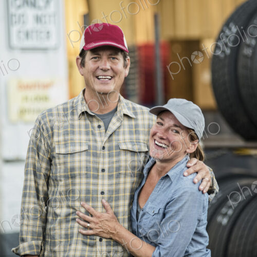 A husband and wife truck driving team near their truck parked in a parking lot at a… A husband and wife truck driving team near their truck parked in a parking lot at a…