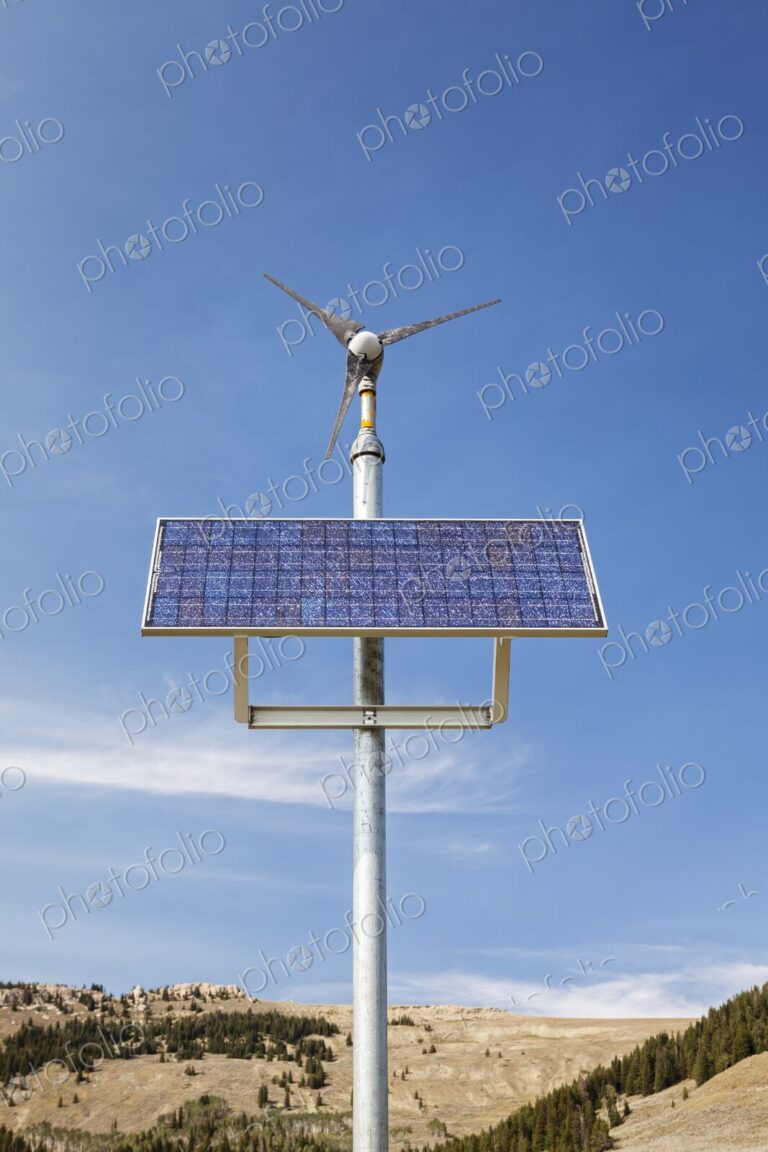 A hybrid solar panel and wind turbine system against a clear blue sky near Manderson,…