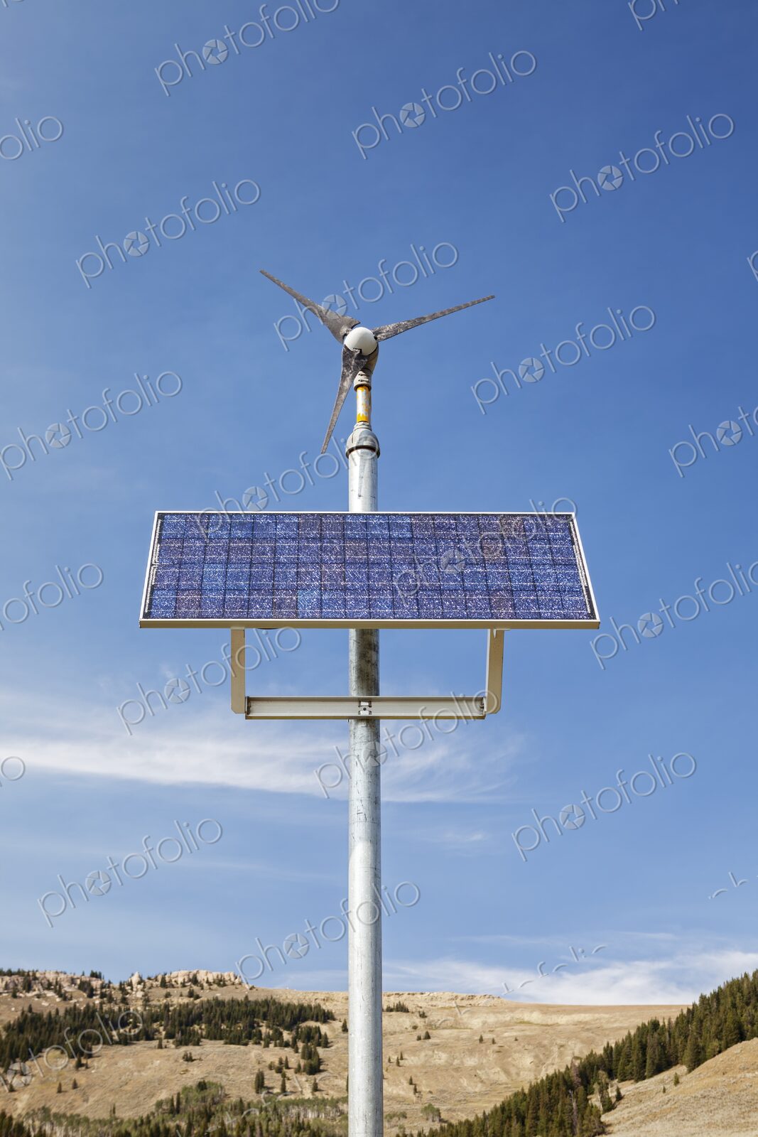 A hybrid solar panel and wind turbine system against a clear blue sky near Manderson,…