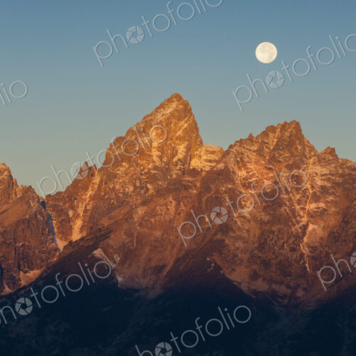 A jagged mountain range in the Grand Teton national park at night, with a full moon in… A jagged mountain range in the Grand Teton national park at night, with a full moon in…