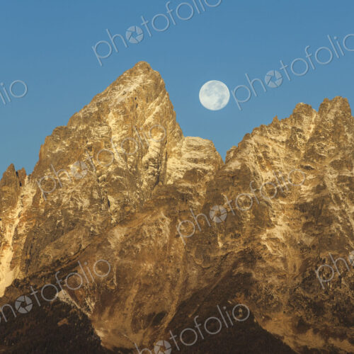 A jagged mountain range in the Grand Teton national park at night, with a full moon in… A jagged mountain range in the Grand Teton national park at night, with a full moon in…