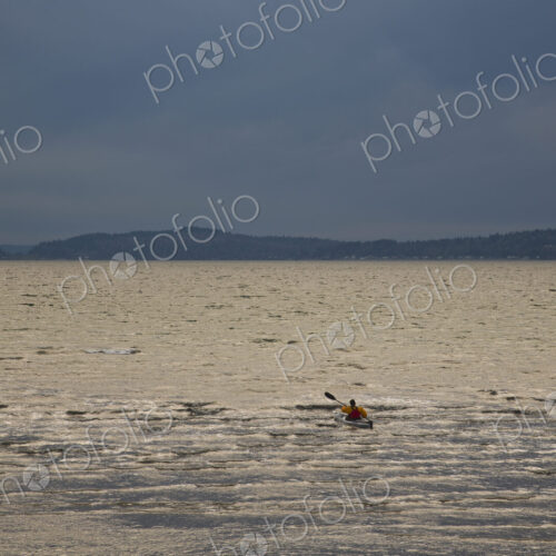 A kayaker paddles his sea kayak in the Puget Sound on a dark and cloudy evening.