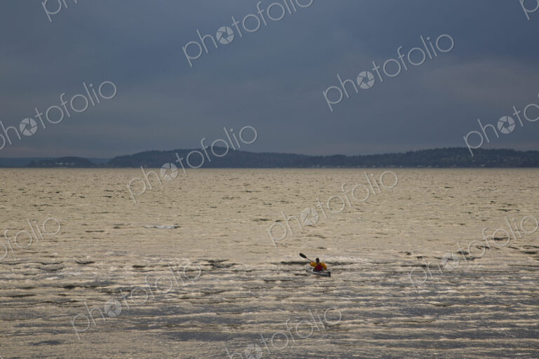 A kayaker paddles his sea kayak in the Puget Sound on a dark and cloudy evening.