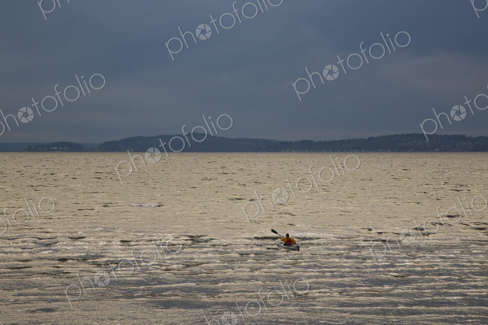 A kayaker paddles his sea kayak in the Puget Sound on a dark and cloudy evening.