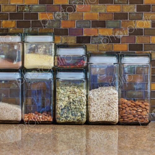 A kitchen in a home with a tiled wall, counter top with food storage containers.