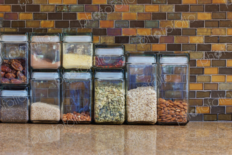 A kitchen in a home with a tiled wall, counter top with food storage containers.