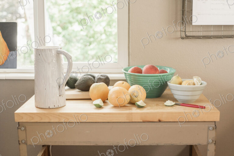 A kitchen table by a window, fresh fruit and avocados in bowls.