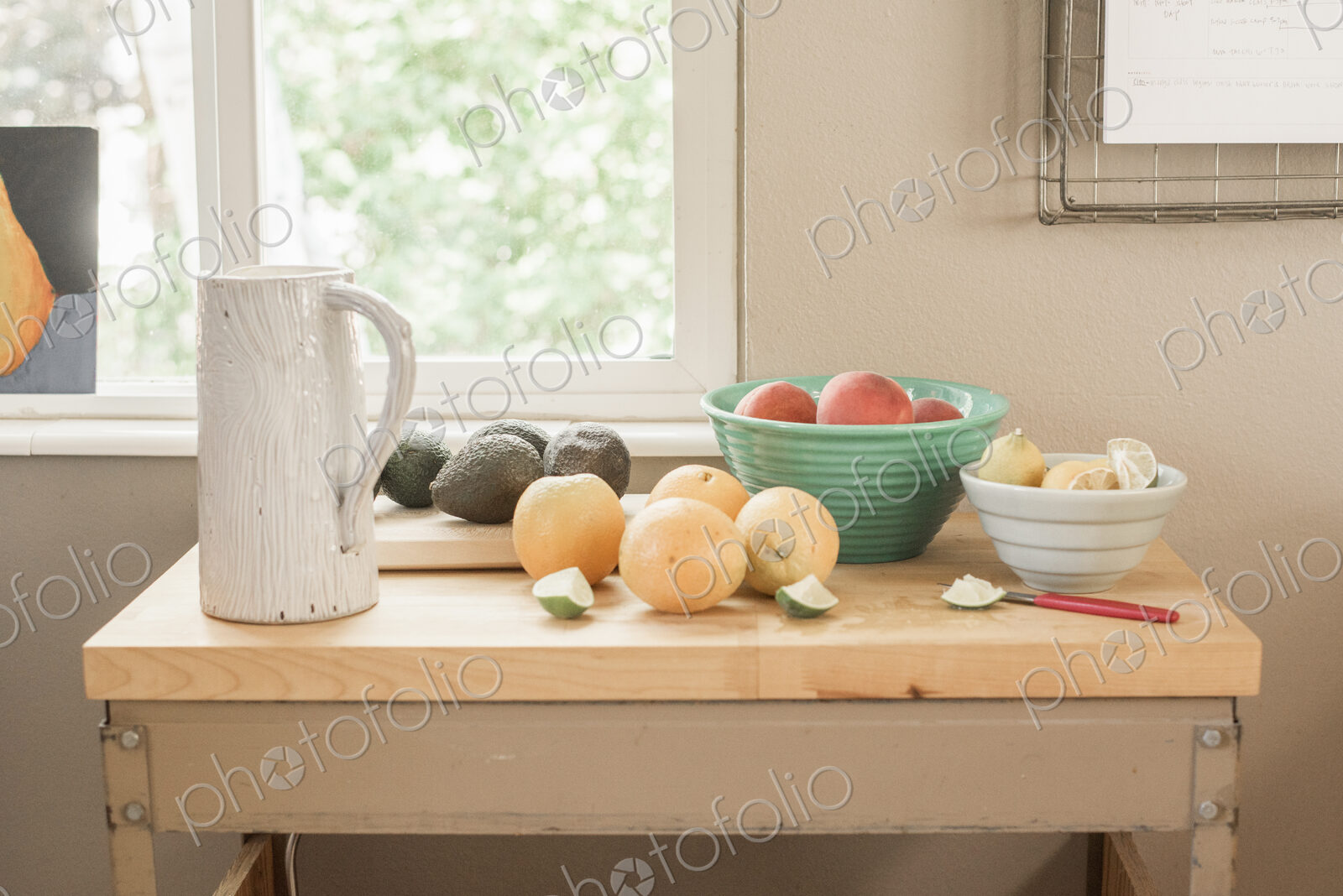 A kitchen table by a window, fresh fruit and avocados in bowls.