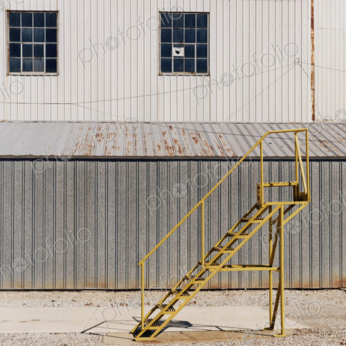 A ladder beside an industrial unit, with corrugated iron walls.