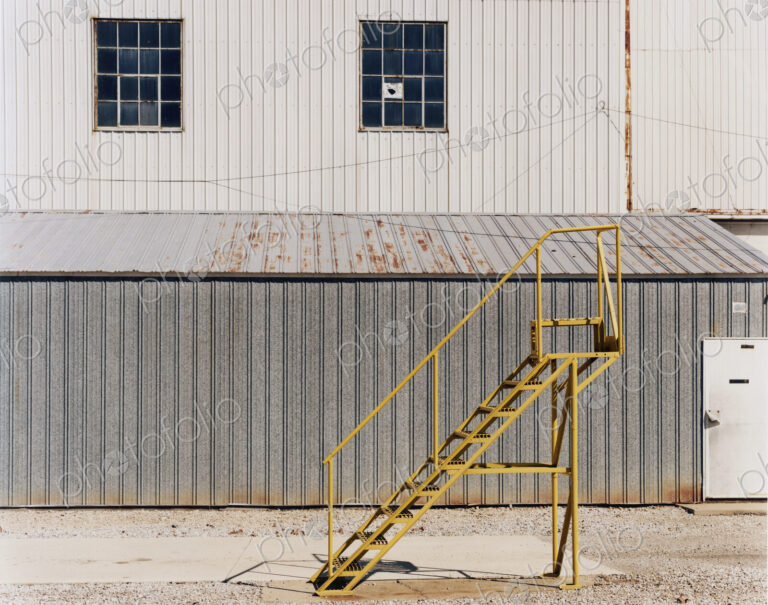 A ladder beside an industrial unit, with corrugated iron walls.