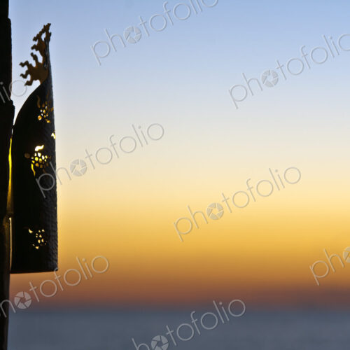 A lantern grille on a wall, silhouette against the sunset sky.