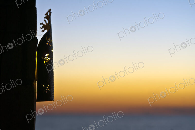 A lantern grille on a wall, silhouette against the sunset sky.