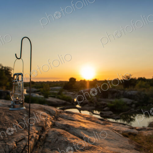 A lantern placed next to a river during sunset.