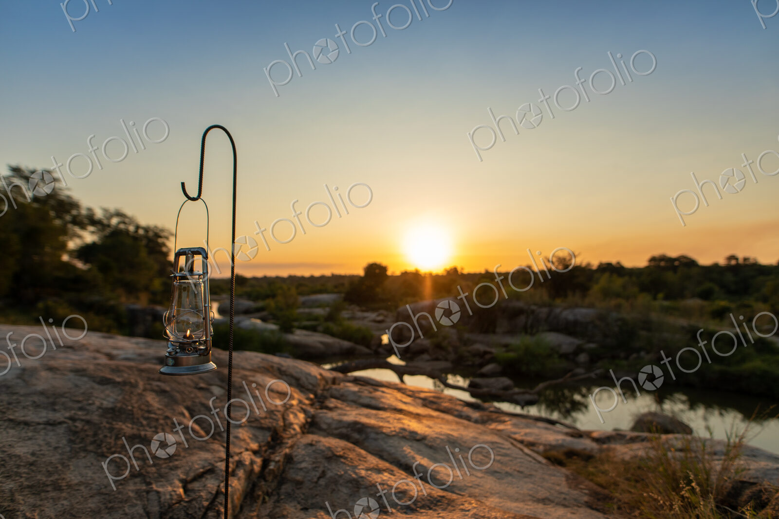 A lantern placed next to a river during sunset.