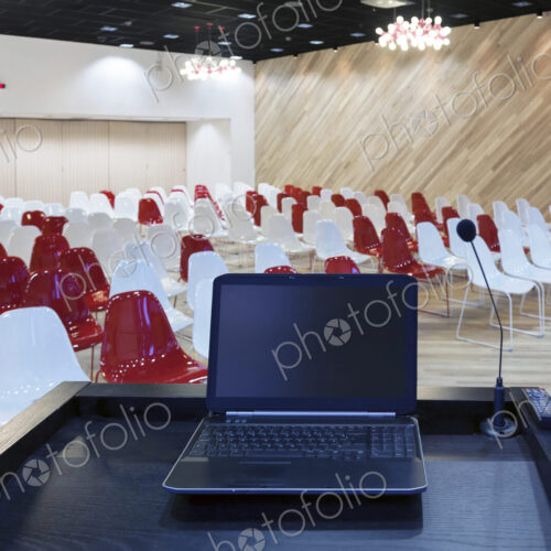 A laptop computer at a podium and rows of chairs in a large room A laptop computer at a podium and rows of chairs in a large room