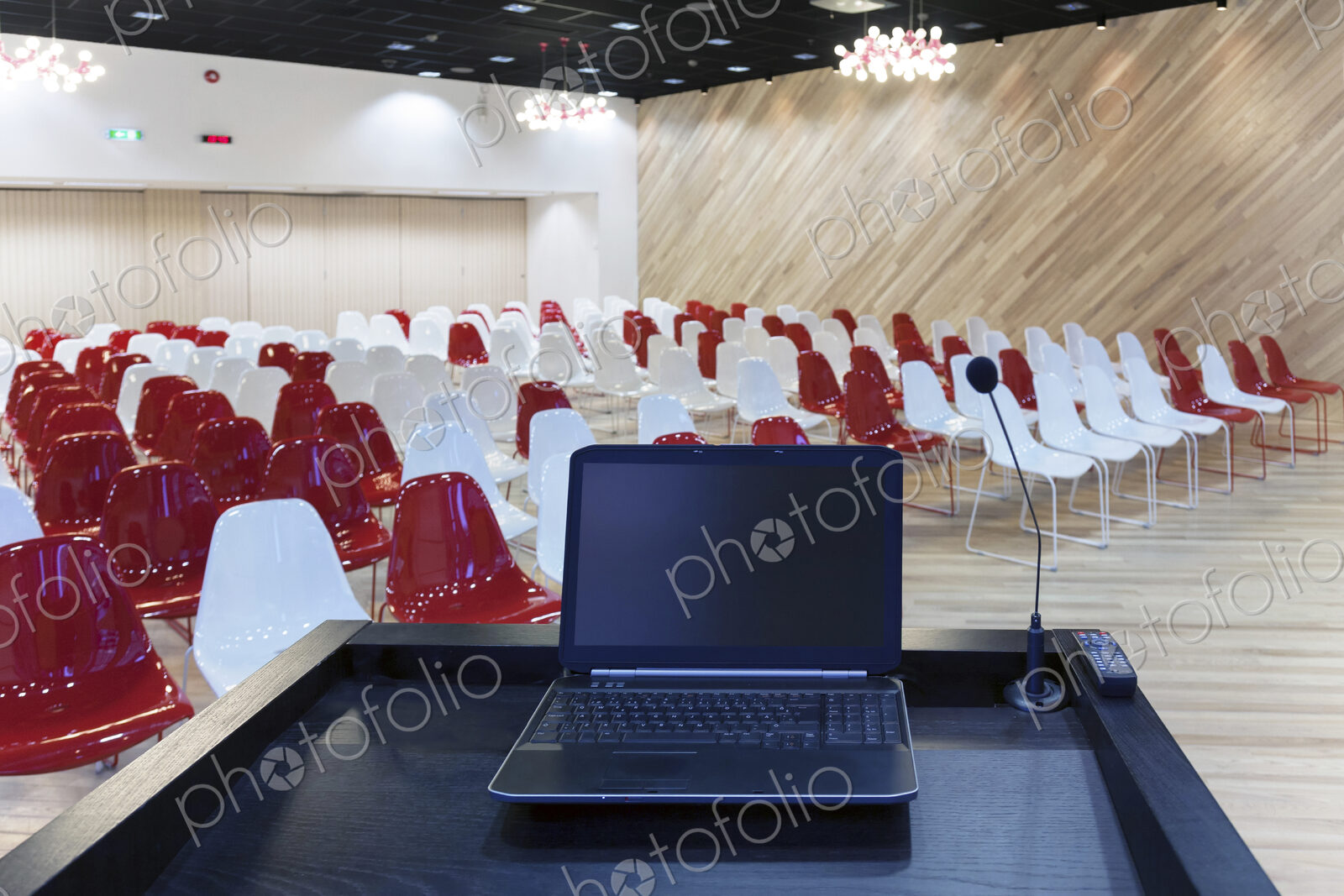 A laptop computer at a podium and rows of chairs in a large room