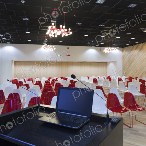 A laptop computer at a podium and rows of chairs in a large room A laptop computer at a podium and rows of chairs in a large room